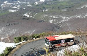 観光客らを乗せて雪の残る岩木山を走る一番バス＝28日午前8時50分ごろ