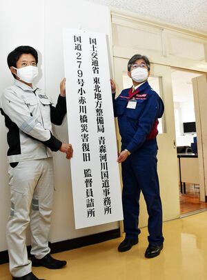 「小赤川橋災害復旧監督員詰所」の看板を掛ける一戸所長（右）と宮下市長