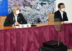 記者会見に臨む桜田市長（左）。市長の前にある透明な板に原稿を映すことができる