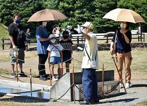 日よけの傘を差しながら三内丸山遺跡の遺構を見学する人たち＝青森市