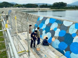 足場に上り防潮堤に壁画を描く学生たち＝2021年9月（八工大提供）