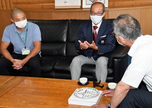 桑田村長（右）に五輪での仕事ぶりを話す矢澤さん（左）と木立さん＝10日、西目屋村役場
