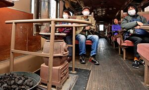 雰囲気のある石炭ストーブの暖かさに笑みがこぼれる観光客ら＝1日、津軽鉄道