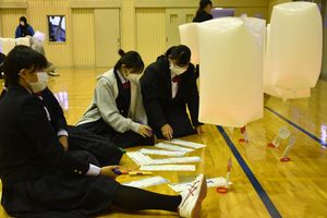 スカイランタン（白い風船）に貼る願い事やメッセージを考える生徒たち＝15日、鶴田高体育館