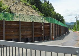 土砂崩れ場所に設置されている高さ約4メートルの仮設防護柵。この脇を車両が通行する＝11日午前、西目屋村砂子瀬