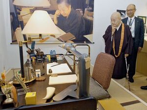 八戸市の「はっち」で開かれた三浦哲郎展で、三浦さん愛用の文机に見入る瀬戸内寂聴さん（右から2人目）。奥の写真が三浦さん＝2011年11月2日
